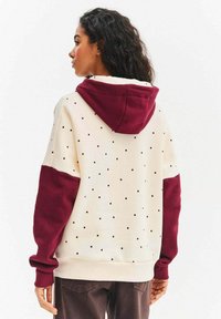 Bluza z kapturem w kolorze kremowym z bordowymi akcentami, z wzorem w kropki. Wykonana z miękkiego materiału, z długimi rękawami i wykończeniami na mankietach.