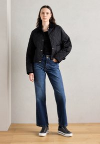 Sort quiltet jakke med en cropped design, knaplukning og sidelommer, kombinert med høyt liv blå denimbukser og grå sneakers.