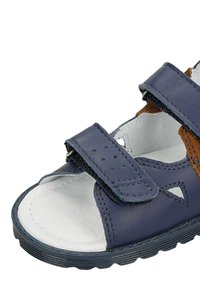 Sandal in pelle blu con due cinturini regolabili in velcro, dettagli perforati e una soletta bianca texturizzata, progettata per il comfort e il supporto.