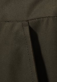 Tissu vert foncé avec une surface texturée, présentant un tissage diagonal et des coutures visibles le long des plis. Aucune motif ou accent distinct.