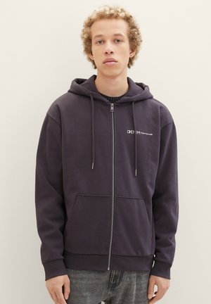 Haut à capuche zippé bleu foncé en mélange de coton, avec une poche frontale, un capuchon à cordon et un logo sur la poitrine gauche. Texture lisse.