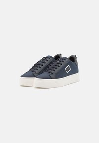 Navy blue sneakers with a textured fabric upper, flat white rubber sole, and dark laces. Features a small logo on the side.