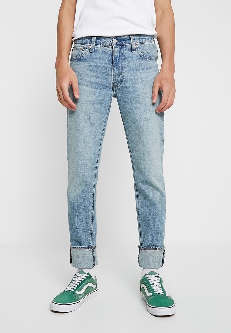 Vaaleansiniset denim-farkut, joissa on kapeampi istuvuus, keskikorkea vyötärö, käännetyt lahkeet ja hillitty haalistuminen. Yhdistetty vihreisiin lenkkareihin.