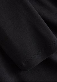 Svart kortärmad tygbit med en slät textur och detaljerade fållar. Fokus ligger på materialets mjukhet.