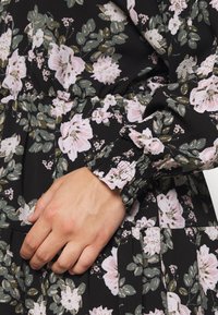 Schwarzes Blumenkleid mit rosa und grünen Blumen, mit gesmokten Bündchen und gerafftem Detail an der Taille. Leichtes, strukturiertes Material.