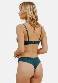 Ensemble de bikini en teal comprenant un bralette texturé avec des bretelles réglables et des accessoires en ton doré, assorti à un bas de bikini taille basse.