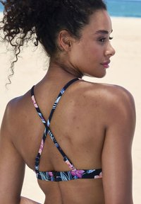 Bikini-top met bloemenpatroon, voorzien van kruislingse bandjes, met roze en blauwe accenten op een marineblauwe achtergrond en een sluiting met haakje op de rug.