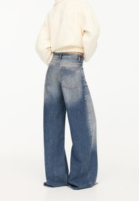 Jeans de mezclilla azul holgados con un lavado desgastado, que presentan una cintura alta, grandes bolsillos traseros y un acabado texturizado. Diseñados para un ajuste relajado.