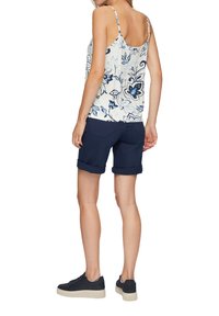 Tanktop mit Blumenmuster und dünnen Trägern, kombiniert mit blauen, umgeschlagenen Shorts und schwarzen Sneakers mit strukturiertem Profil. Rückansicht.
