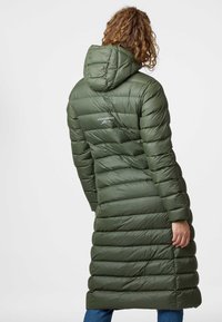 Vadderad lång jacka i mörkgrön med huva. Har ett horisontellt kviltat mönster, logotyp på baksidan och avslappnad passform. Vågad fåll.