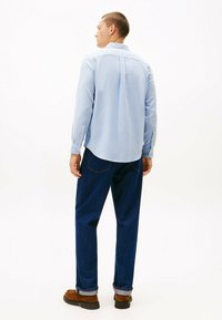 Lys blå langærmet skjorte med knappede manchetter, parret med mørkeblå denimjeans og brune ruskindssko. Bag udsigt. Glat stof tekstur.