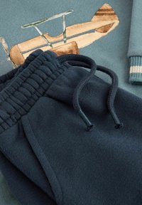 Cotton sweatshirt in muted teal with a vintage airplane print, paired with navy fleece joggers featuring an elastic waistband and drawstring.