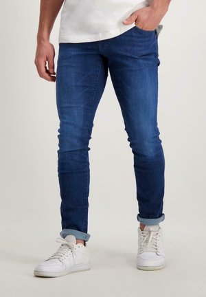 Blauwe slim-fit jeans van denim, met een normale taille, omgeslagen pijpen en zijzakken. Draagt witte sneakers.