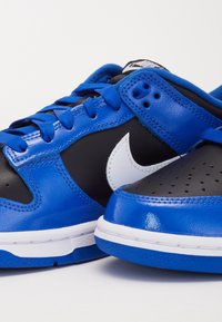 Baskets Nike avec une tige en cuir bleu et noir, arborant un swoosh blanc, des perforations rondes et des lacets bleus. Texture lisse et semelle rembourrée.