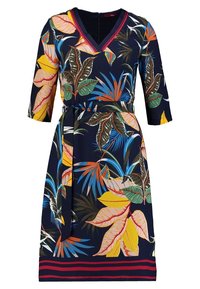 Marinblå klänning med v-ringning, trekvartsärmar och midja med bälte. Har ett livligt tropiskt bladmönster i gult, grönt och blått.