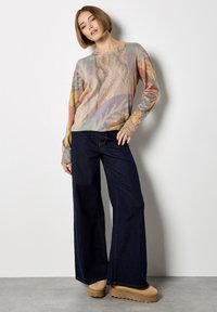 Sweter z dzianiny z kolorowym kwiatowym wzorem w pastelowych odcieniach. Połączony z ciemnymi, szerokimi spodniami dżinsowymi i jasnobrązowym obuwiem na platformie.