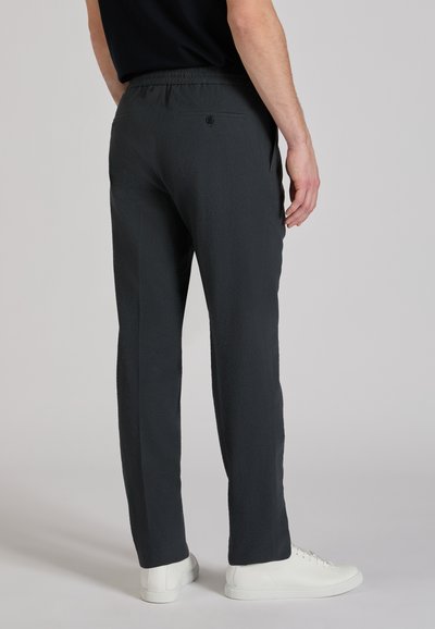 Dark gray trousers with a textured fabric, elastic waistband, and back pocket detail, worn with white sneakers.