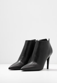 Sorte læder ankelstøvler med spids tå, slankt design og stilettohæle. Glat tekstur og minimalistisk lynlåsforsegling bagpå.