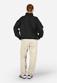 Melna pārmērīga izmēra sporta krekls ar augstu apkakli, saskaņots ar krēmkrāsas sporta biksēm ar elastīgām aprocēm. Ievērojamas kurpes ir baltas ar melnām svītrām.