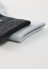 Zwei Paare gefalteter Socken, ein dunkelgraues und ein hellgraues, liegen auf einer weißen Fläche.