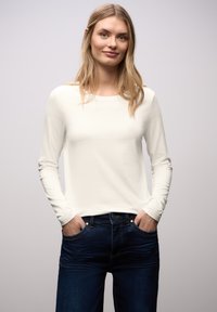 Letvægts cremefarvet skjorte med lange ærmer og afrundet halsudskæring, kombineret med mørkeblå jeans med klassisk fem-lomme design og diskret søm.