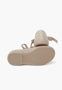 Zapatillas de malla beige con una superficie texturizada, suela de goma plana y correas de tela. Presenta detalles de marca en la suela.