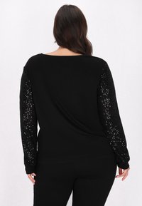 Maglietta nera a maniche lunghe con dettagli di paillettes nere luccicanti sulle maniche, tessuto morbido e una vestibilità rilassata con scollo a barchetta.