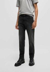 Vaqueros de denim negro con un ajuste slim, diseño de cinco bolsillos y ligero desgastado. Combinados con una camiseta de manga corta gris y botas negras con cordones.