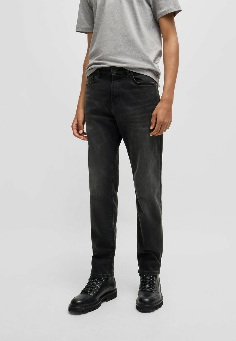Vaqueros de denim negro con un ajuste slim, diseño de cinco bolsillos y ligero desgastado. Combinados con una camiseta de manga corta gris y botas negras con cordones.