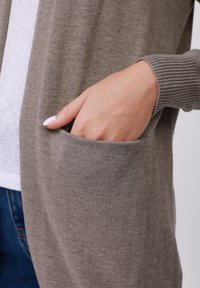 Gray knit cardigan featuring ribbed cuffs and a side pocket. Soft, textured fabric with a relaxed fit. Visible inner layer in white.