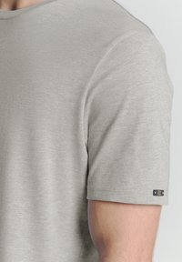 Grijze T-shirt met korte mouwen van zachte stof. Heeft een ronde halslijn en een klein zwart accentlabel op de mouw.