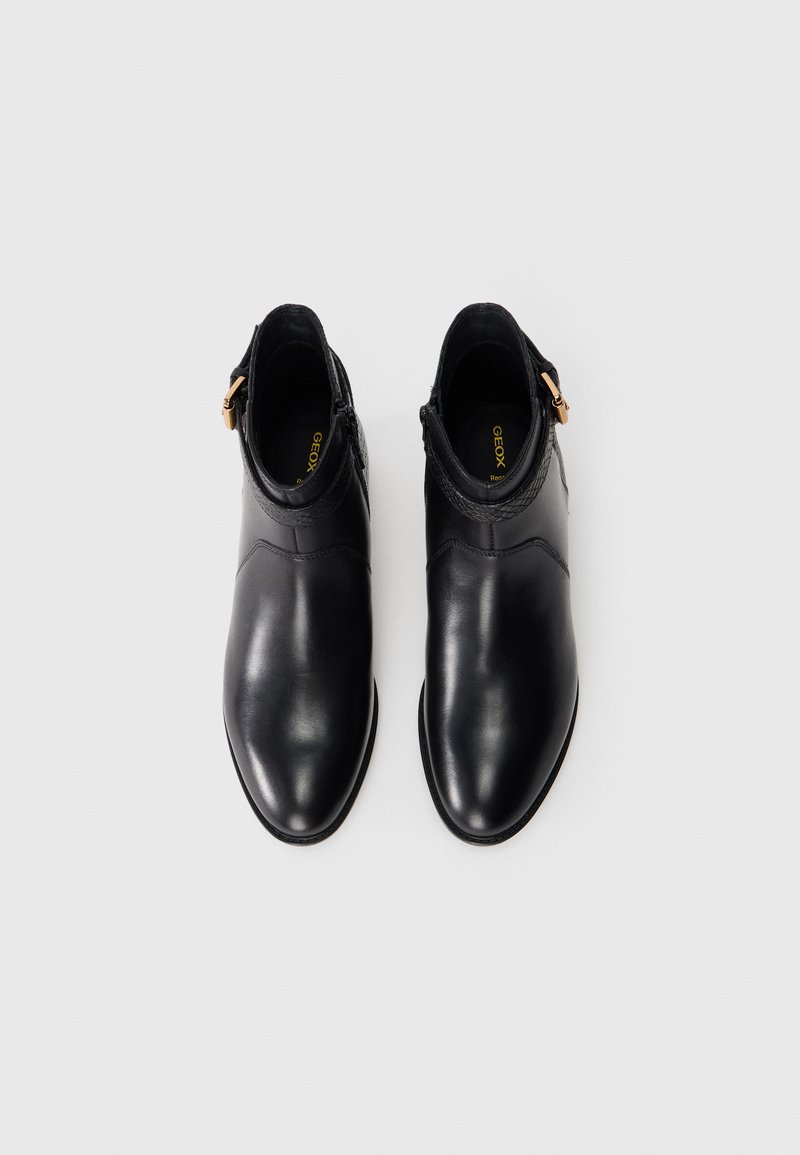 Bottes chelsea en cuir noir avec une finition lisse, bout pointu, fermeture éclair sur le côté et accents texturés au niveau du col. Marque Geox visible à l'intérieur.