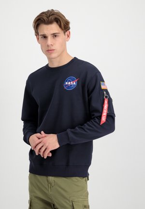 Navyblaues Sweatshirt mit NASA-Logo. Gerippter Rundhalsausschnitt, eingerollte Ärmel und eine aufgesetzte Tasche am Arm mit roten Reißverschlussdetails.