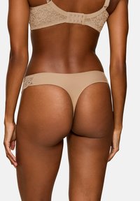 Nude koronkowe stringi z półprzezroczystym tyłem i gładkim przodem, z misternymi detalami koronkowymi po bokach oraz standardowym pasem.