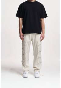 Svart bomulls-t-shirt med avslappnad passform, kombinerad med lätta beige cargobyxor med flera fickor, bärs med vita sneakers.