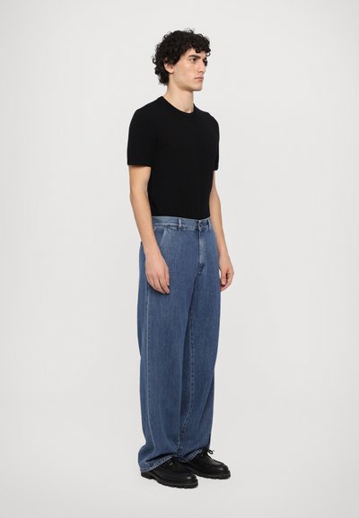 Black short-sleeve t-shirt paired with wide-leg blue jeans and black lace-up shoes, displayed against a plain light background.