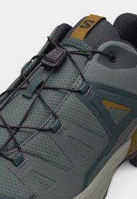 Γκρι και πράσινο παπούτσι πεζοπορίας με σύστημα γρήγορου δέσιμου και μαύρο κουμπί σε αναπνεύσιμο πλέγμα επάνω μέρος και μαξιλαρωμένο γιακά.