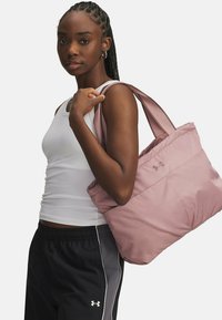 Pink quilted tote bag with a soft texture and wide straps, held under the arm. Features an Under Armour logo on the front.