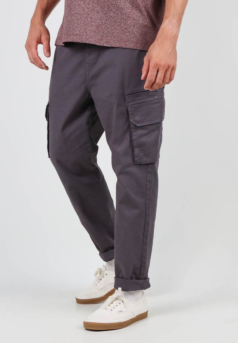 Pantalons cargo en coton gris foncé, dotés de plusieurs poches latérales, d'une coupe décontractée et de poignets retroussés. Associés à des baskets blanches.