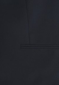 Marinblå kostymtyg med en slät textur. Har en subtil sömdetalj och en enkel ficköppning. Ren, minimalistisk design.