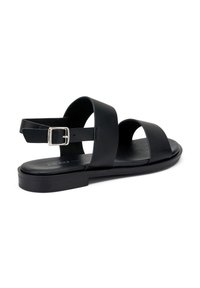Sandali in pelle nera con cinturini larghi, fibbia regolabile alla caviglia, suola piatta e texture liscia. Design semplice con dettagli minimi.