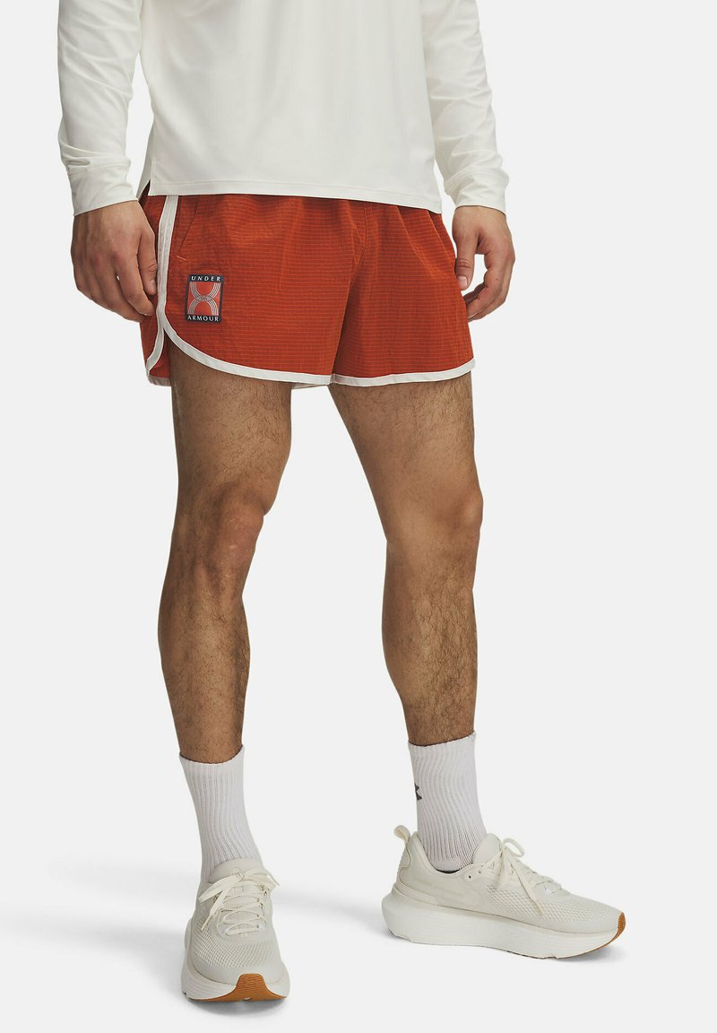 Rote Sportshorts mit weißen Details und einem Under Armour Logo-Patch. Tragen mit einem langärmligen weißen Oberteil und weißen Sneakers.