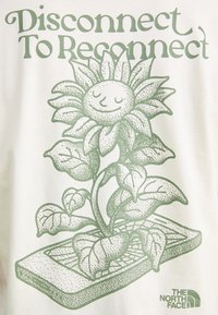 White t-shirt featuring green illustration of a smiling sunflower with leaves and text “Disconnect To Reconnect.” Includes logo for The North Face.