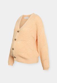 Stickad cardigan i ljus persika med V-ringning, med fem stora knappar och texturerade vågmönster på tyget.
