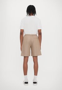 Beige avslappnade shorts med elastisk midja och bakficka, åtföljt av en enkel vit t-shirt och vita strumpor med svarta accenter.