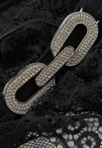 Tela de encaje negra con un gran broche de eslabones de cadena plateada, adornado con piedras de strass transparentes para un detalle y textura adicionales.