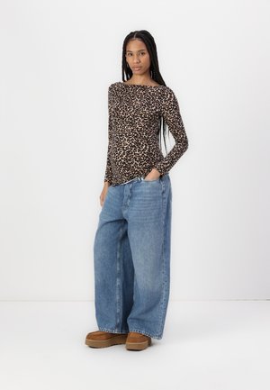 Langsleeve luipaardprint top, gecombineerd met losse, lichtblauwe denim jeans. Model draagt bruine platform schoenen. Eenvoudige, neutrale achtergrond.