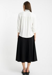 Biała bluzka z rękawami do trzech czwartej i plisowanym tyłem, połączona z czarną spódnicą midi. Zestaw charakteryzuje się gładką fakturą i klasycznym wzornictwem.