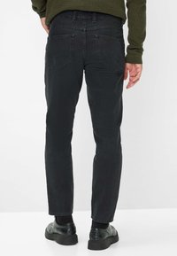 Jeans in denim nero con taglio dritto, dotati di due tasche posteriori e una trama sottile. Indossati con scarpe nere, di spalle rispetto alla fotocamera.