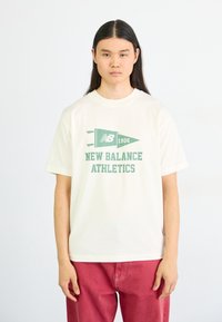 Camiseta de algodón blanca con un diseño impreso en verde que incluye un pennant y el texto "NEW BALANCE ATHLETICS" en letras gruesas.